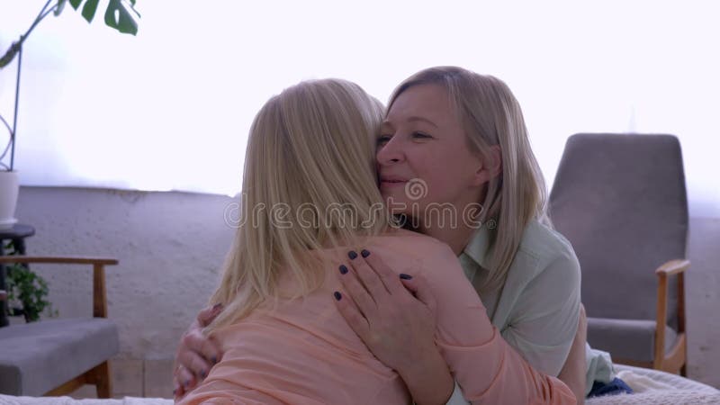 Материнская забота, усмехаясь мать с взрослой дочерью обнимает пока беседующ дома